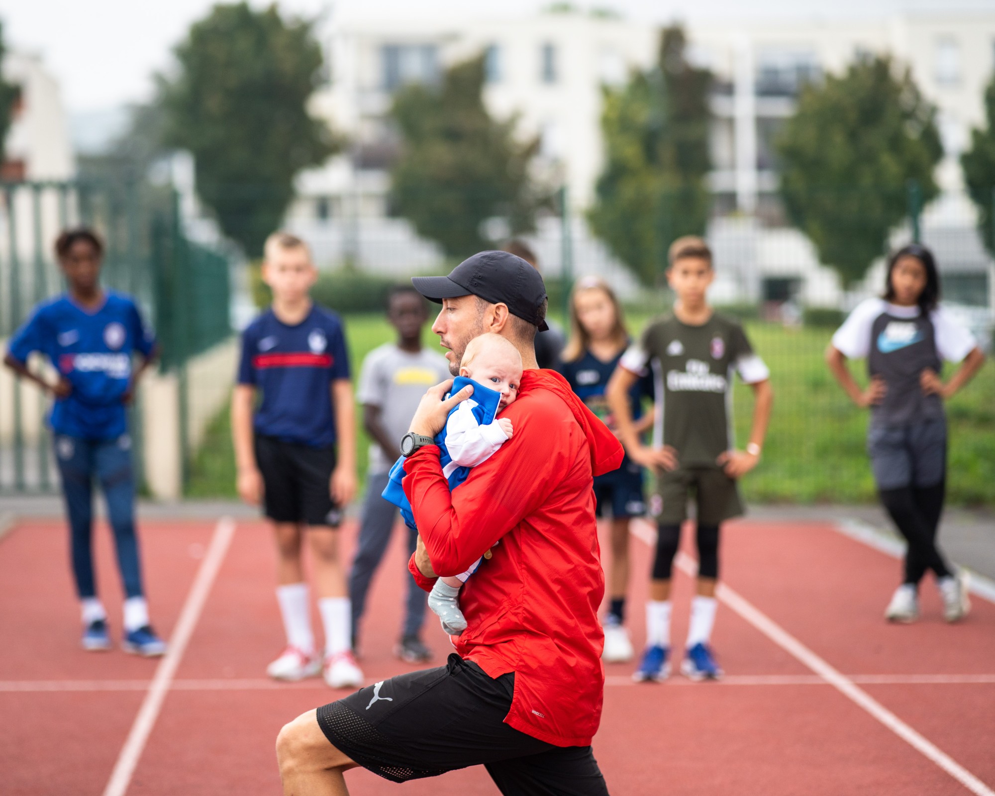 Séance de jeunes athlètes sur la piste, le coach un bébé dans les bras
